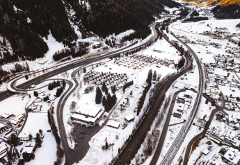 Vista aérea de un lodge en invierno, rodeado de carreteras nevadas, casas, árboles y montañas nevadas.