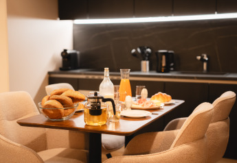 Mesa de desayuno acogedora en una cabaña con pan fresco, jugo, té y huevos en una cocina moderna.
