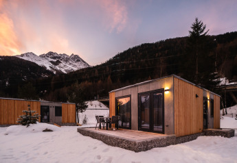 Chalets modernes en bois dans un paysage de montagne enneigée au coucher du soleil, avec terrasse aménagée.