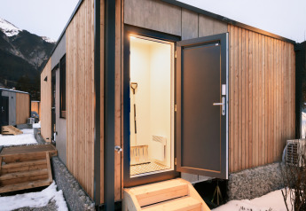 Entrée d’un lodge moderne en bois avec porte ouverte, vue sur la neige et les montagnes en arrière-plan.