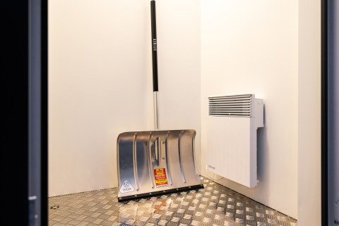 Foto van een metalen schep en een muurkachel in de hoek van een modern lodge met metalen vloer.