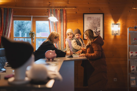 Gezin checkt in bij de receptie van een knusse houten lodge, geholpen door personeel in het winterseizoen.