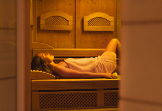 Kvinde slapper af indpakket i et håndklæde, liggende i en sauna på et hyggeligt lodge med træinteriør.