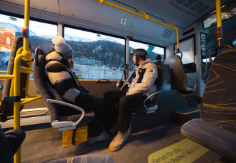 Deux personnes en manteaux d'hiver sont assises face à face dans un bus, montagnes enneigées à l'extérieur.