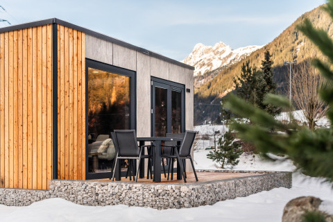 Stanzertal Cabin ved Austriaparks Camping Arlberg i sneklædte østrigske bjerge, terrasse og stole.