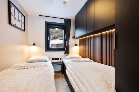 Moderne hytte-soveværelse med to enkeltsenge, trægulv og hyggelig belysning på Stanzertal Cabin i Østrig.
