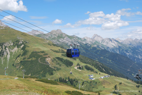 Funivia sopra le Alpi austriache vicino alla Stanzertal Cabin, colline verdi e cielo azzurro visibili.