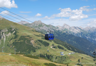 Cable car gliding above the Austrian Alps near Stanzertal Cabin, with green hills and blue skies beyond.