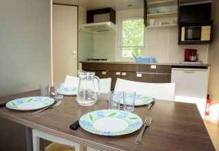 Table dressée avec assiettes, verres et carafe d'eau dans la cuisine moderne d'un mobil-home lumineux.