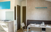 Interior de una casa móvil con zona de comedor, mesa puesta, cocina moderna y suelo de aspecto madera.
