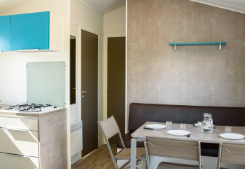 Interior de una casa móvil con zona de comedor, mesa puesta, cocina moderna y suelo de aspecto madera.
