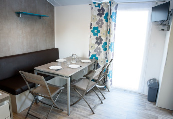 Moderne spiseplads i en mobilhome med fire stole, bænk, borddækning og farverige gardiner.