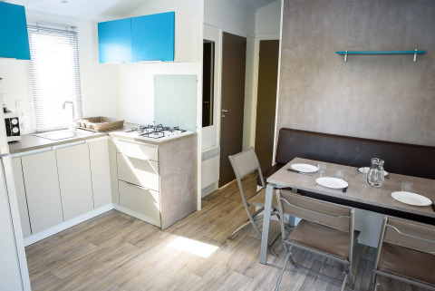 Cuisine-salle à manger moderne et lumineuse dans un mobil-home avec table, quatre chaises et banquette.