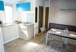 Cuisine-salle à manger moderne et lumineuse dans un mobil-home avec table, quatre chaises et banquette.
