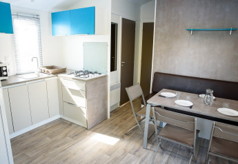 Lyst og moderne køkken-alrum i en mobilhome med spisebord, fire stole og minimalistisk indretning.