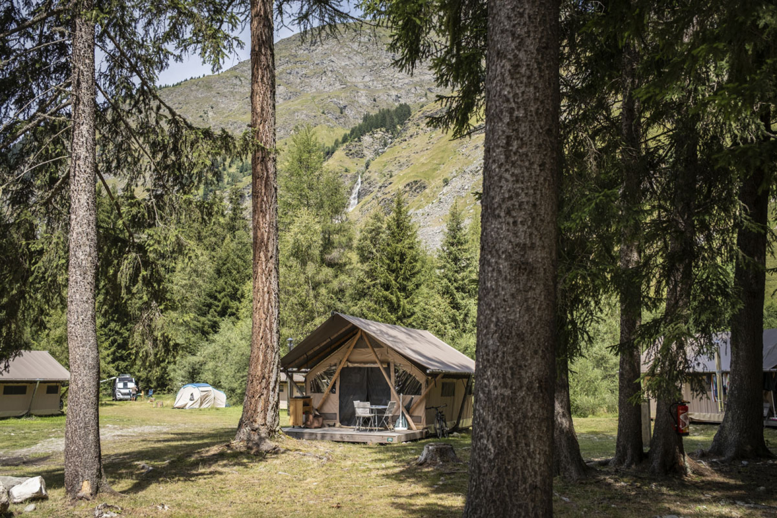 Safaritent 'Tent Canadienne' op een bosrijke camping met uitzicht op bergen en natuurrijke omgeving.