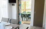 Interiør af en mobilhome med spisebord, stole og åbne døre ud til overdækket terrasse med siddepladser.