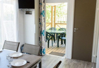 Interno di una casa mobile con tavolo da pranzo, sedie e porta aperta su terrazza coperta con posti a sedere.