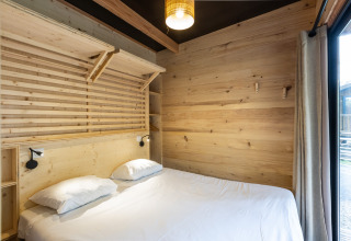 Soveværelse i Mobile Home Vancouver på Huttopia Divonne Les Bains med træpaneler og dobbeltseng.