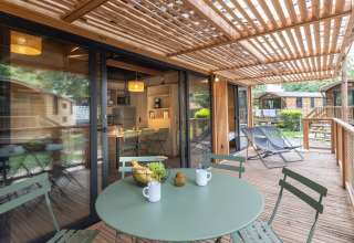 Træterrasse med spisebord på Mobile Home Vancouver ved Huttopia Divonne Les Bains, Frankrig, omgivet af natur.