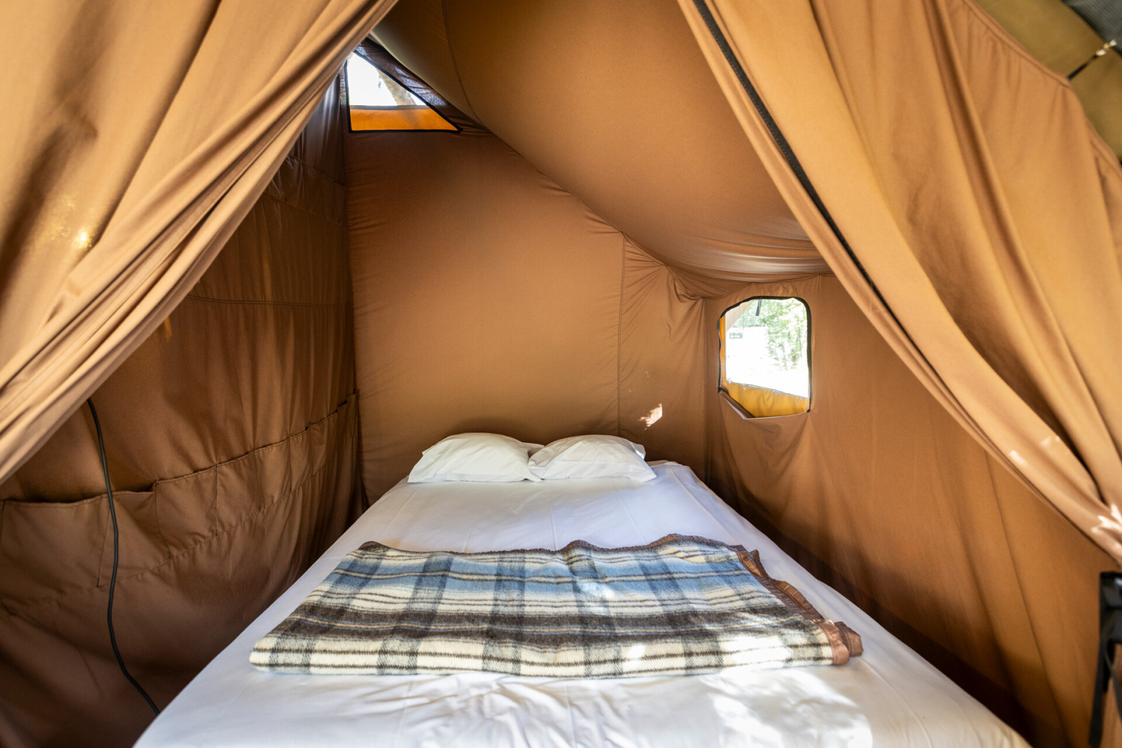 Interieur van een sfeervolle safaritent met tweepersoonsbed en deken bij Huttopia Champagny en Vanoise in Frankrijk.
