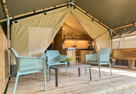 Aménagement intérieur d’une tente safari avec terrasse en bois, chaises bleues, table et cuisine équipée.