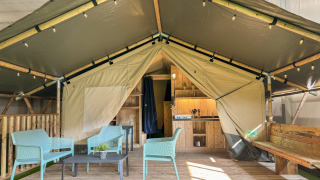 Safaritent met sanitaire voorzieningen, houten terras, moderne zitjes en open keukenruimte.