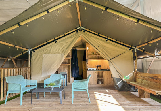 Safaritent met sanitaire voorzieningen, houten terras, moderne zitjes en open keukenruimte.