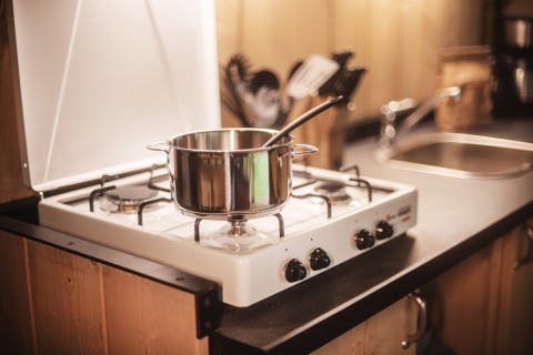A pot with a spoon sits on a gas stove in a cozy kitchen at the Safari tent at Emmerbølle Strand Camping, Denmark.