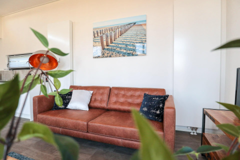 Zithoek in tiny house Cube Exclusive Plus bij EuroParcs Bad Meersee met bruine sofa en wanddecoratie.
