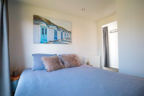 Slaapkamer in de Cube Exclusive Plus tiny house bij EuroParcs Bad Meersee met blauw bedlinnen en kustfoto.