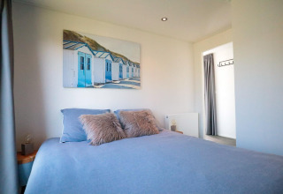 Bedroom in Cube Exclusive Plus tiny house at EuroParcs Bad Meersee featuring blue bedding and seaside art.