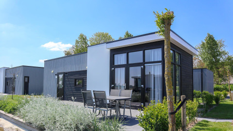 Moderne tiny house Cube La Mer 4 met grote ramen, buitenterras met eettafel en groene tuin op een zonnige dag.