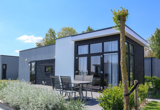 Moderne tiny house Cube La Mer 4 met grote ramen, buitenterras met eettafel en groene tuin op een zonnige dag.