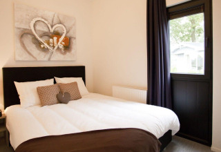 Moderne slaapkamer in tiny house Cube La Mer 4, EuroParcs Bad Meersee, Nederland, met raam en schilderij.