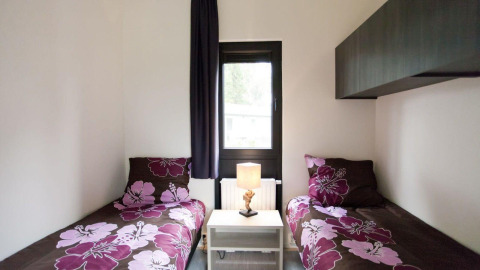 Slaapkamer met twee eenpersoonsbedden, bloembeddengoed, lamp en raam in Cube La Mer 4, EuroParcs.