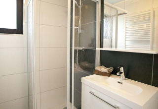Moderne badkamer met douche, witte wastafel en spiegel in Cube La Mer 4 op EuroParcs Bad Meersee.