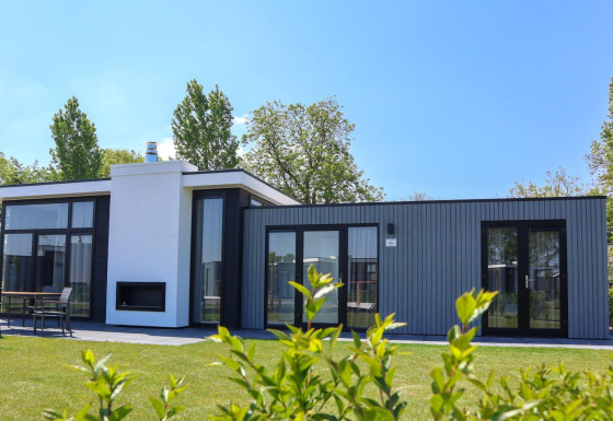 Moderne tiny house Cube Exclusive 4 met grote ramen en terras, omgeven door gras en bomen op een zonnige dag.