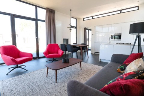 Moderne woonkamer in Cube Exclusive 4 tiny house op EuroParcs Bad Meersee met rode stoelen en grote ramen.