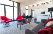 Moderne woonkamer in Cube Exclusive 4 tiny house op EuroParcs Bad Meersee met rode stoelen en grote ramen.
