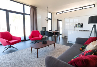 Moderne woonkamer in Cube Exclusive 4 tiny house bij EuroParcs Bad Meersee met rode stoelen en grote ramen.