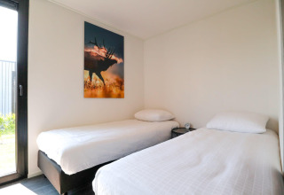 Moderne slaapkamer met twee eenpersoonsbedden, wit beddengoed, hertenfoto aan de muur en daglicht.