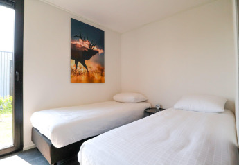 Modernes Schlafzimmer mit zwei Einzelbetten, weißer Bettwäsche, Hirschbild an der Wand und Tageslicht.