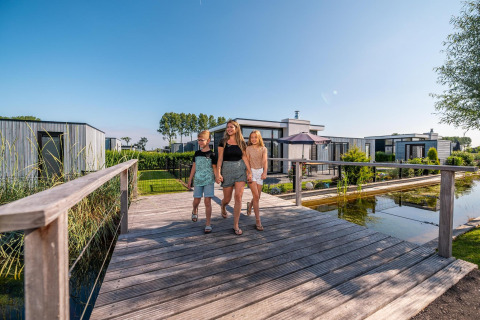 Gezin loopt over houten brug bij Cube Exclusive 4 tiny house in EuroParcs Bad Meersee, Nederland.