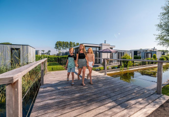 Famiglia che cammina su un ponte davanti alla tiny house Cube Exclusive 4 a EuroParcs Bad Meersee, Paesi Bassi.