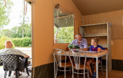 Older man and boy chatting inside a safari tent at De Tien Heugten, Netherlands, with greenery outside.