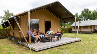 Five people relax on a deck in front of a safari tent at Safaritenten Familieverblijf campsite.