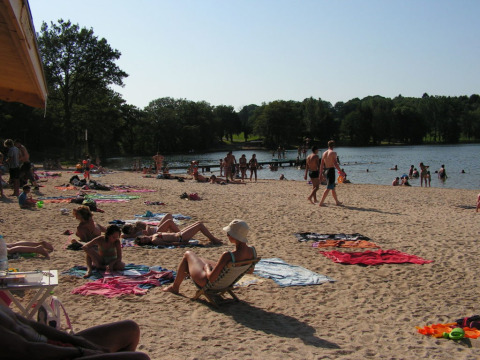 Persone si rilassano sulla spiaggia sabbiosa e nuotano nel lago al campeggio Seasonova Lac de Bournazel.