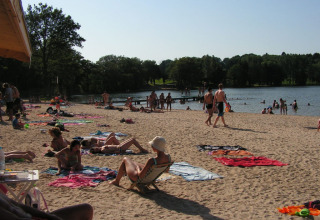 People relaxing on the sandy beach and swimming in the lake at Campsite Seasonova Lac de Bournazel, France.