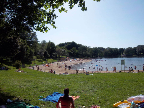 Lakeside beach with swimmers and sunbathers at Campsite Seasonova Lac de Bournazel in Nouvelle-Aquitaine, France.